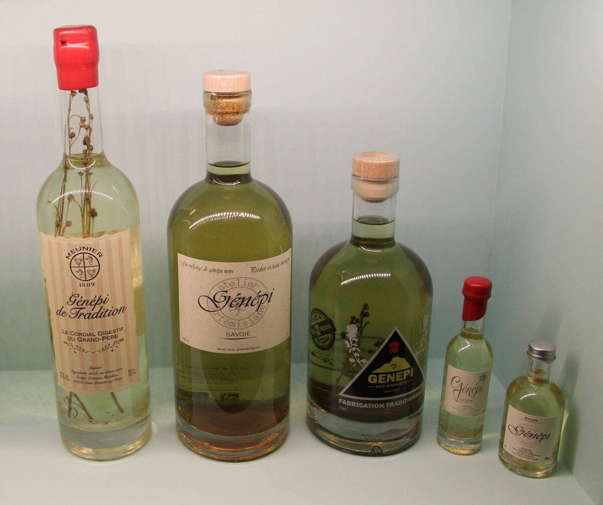Bottles of Génépi, the green herbal liqueur, lined up on a shelf against a pale green background