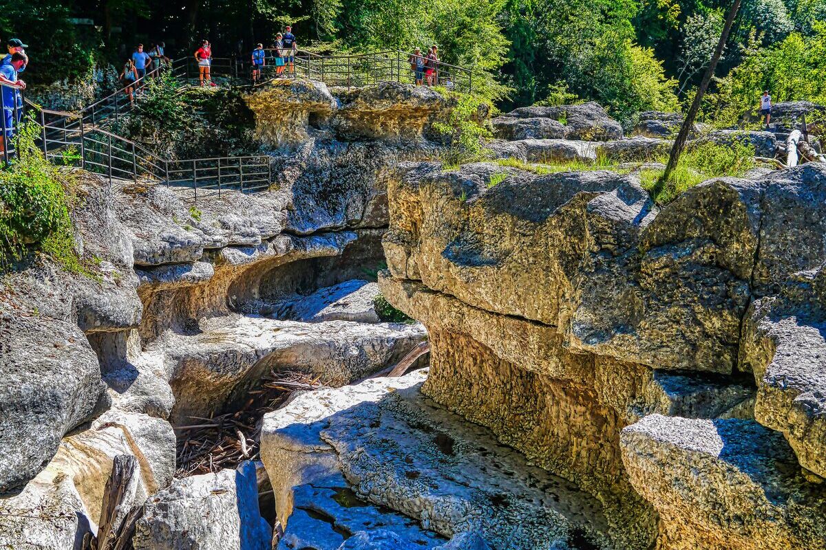 Visitors on the railed walkway above the Mer des Rochers in the Gorges du Fier, with smooth carved limestone blocks below and green forest above
