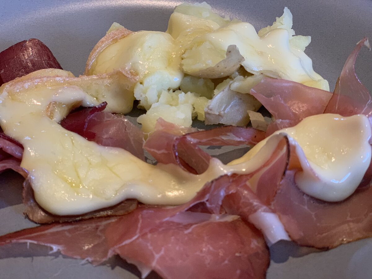 Melted raclette cheese poured over slices of cured ham and boiled potatoes on a plate