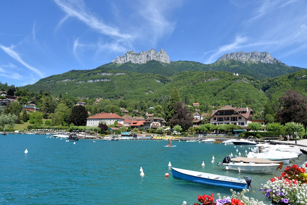 The Talloires waterfront with moored boats, flower boxes on the quay and limestone peaks rising above the village