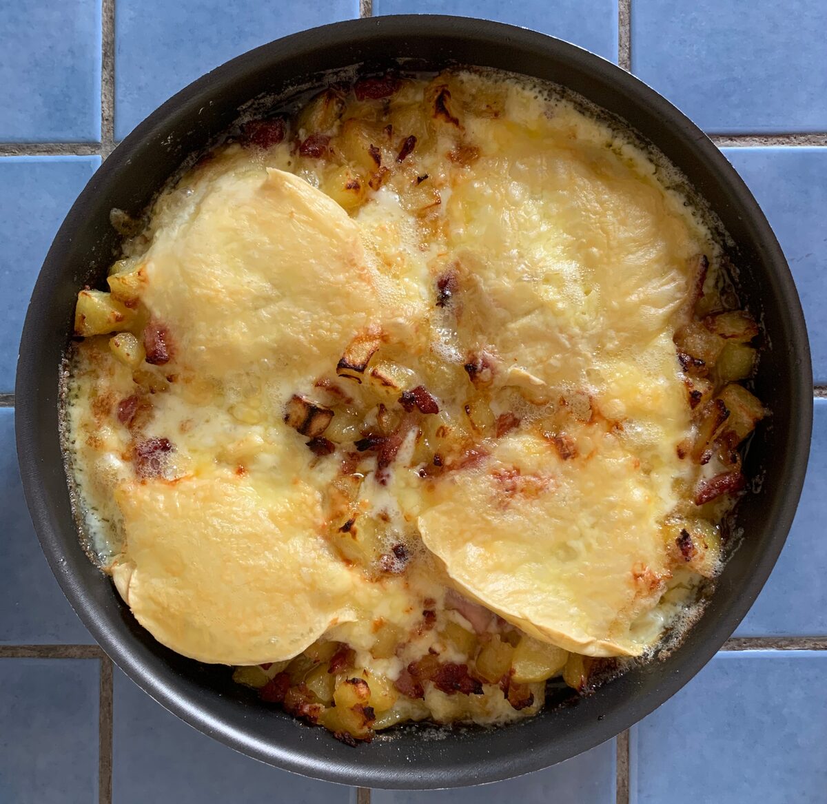 A tartiflette in a round dark dish, with diced potatoes and lardons under two browned, melted rounds of Reblochon