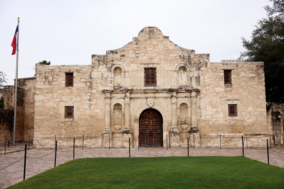 The limestone front of the Alamo mission chapel in San Antonio with its carved doorway and a Texas flag