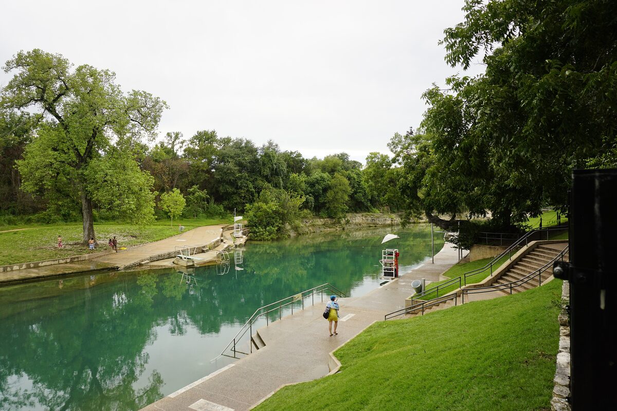 The green spring-fed water of Barton Springs Pool with a grassy bank and a lifeguard chair