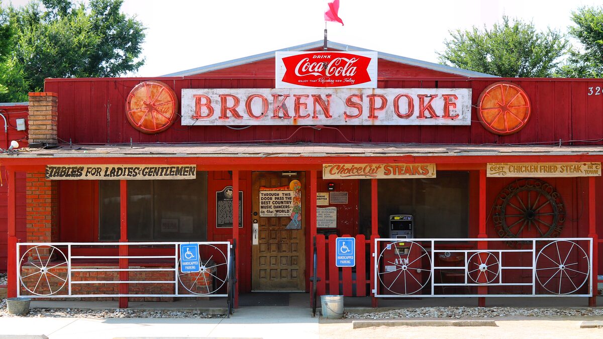 The red wooden front of the Broken Spoke dance hall with its Coca-Cola sign and wagon-wheel railings