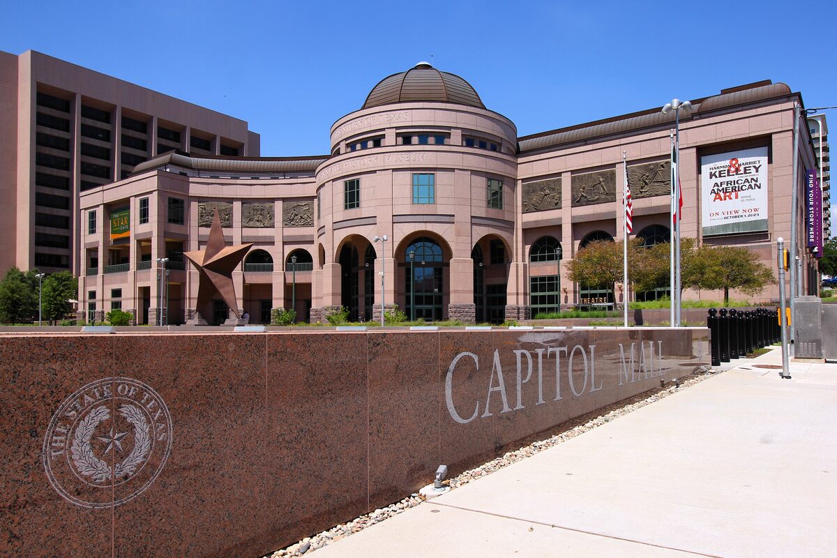 The pink granite front of the Bullock Texas State History Museum with its rotunda and the Capitol Mall wall in front