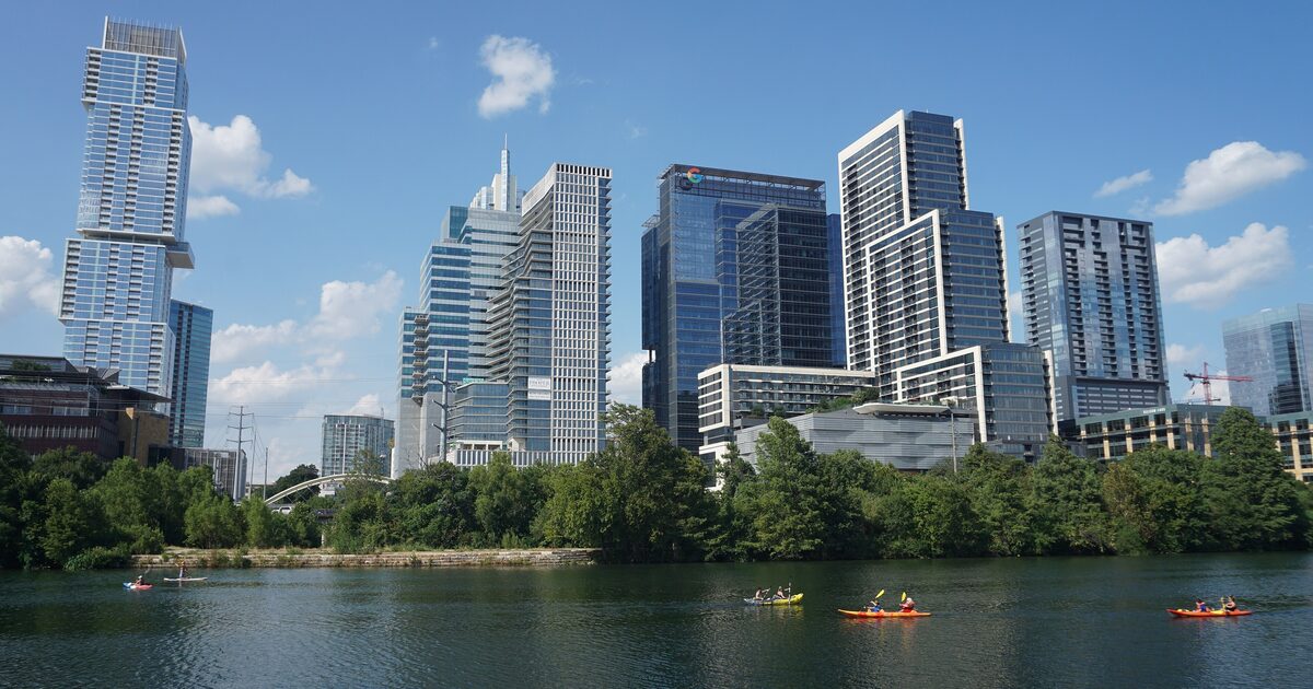 The downtown Austin skyline seen across Lady Bird Lake on a sunny day, with kayakers on the water