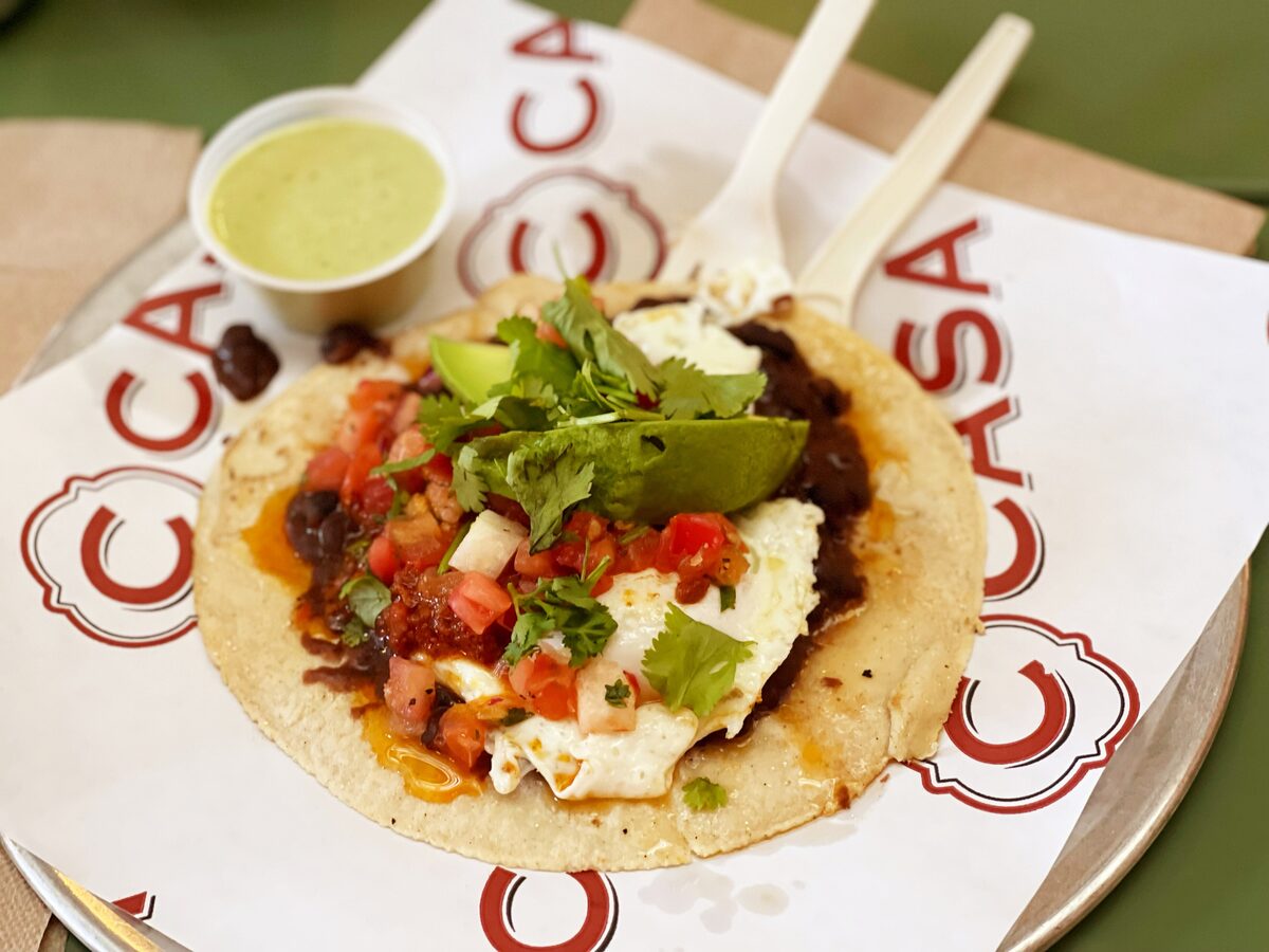 A breakfast taco on a flour tortilla with egg, black beans, pico de gallo and avocado, and a cup of green salsa