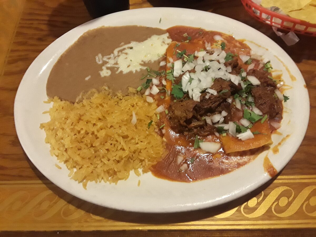 A plate of beef enchiladas with onion and cilantro, refried beans and rice