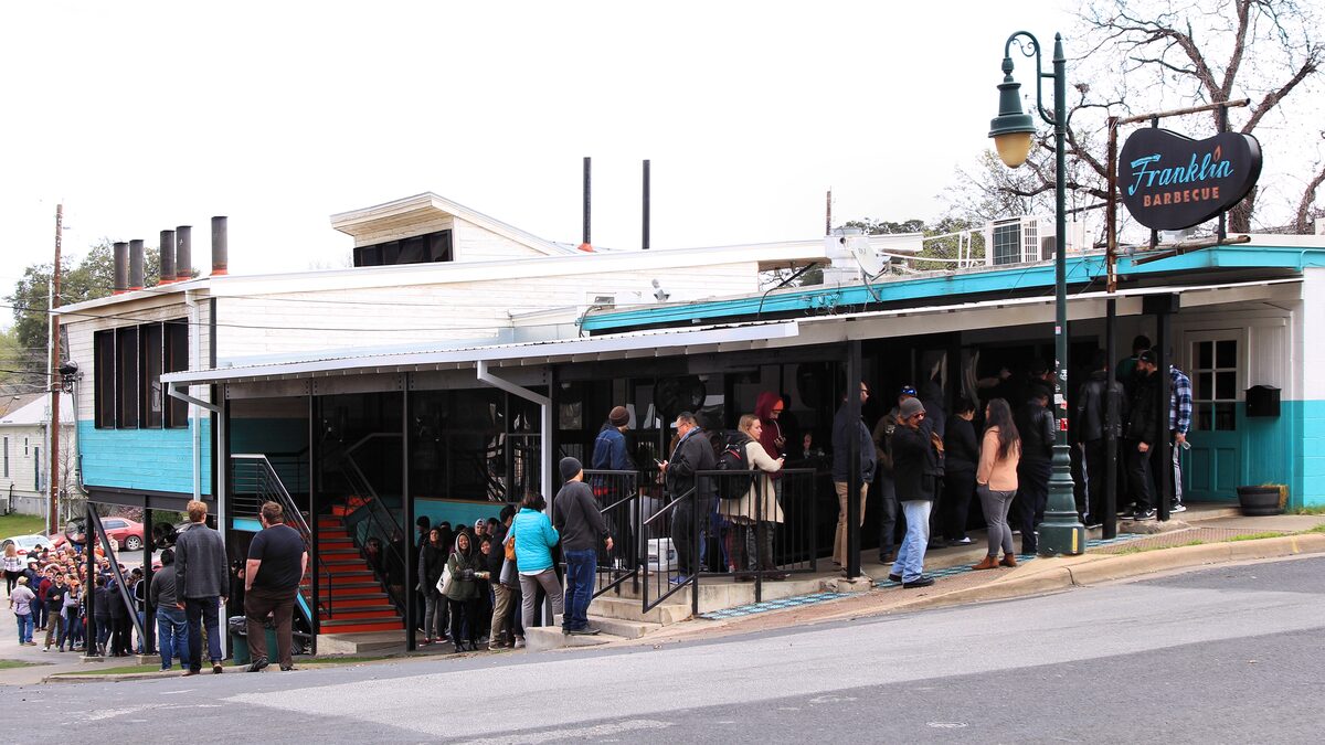 The queue of customers on the steps outside Franklin Barbecue, with its teal trim and Franklin sign