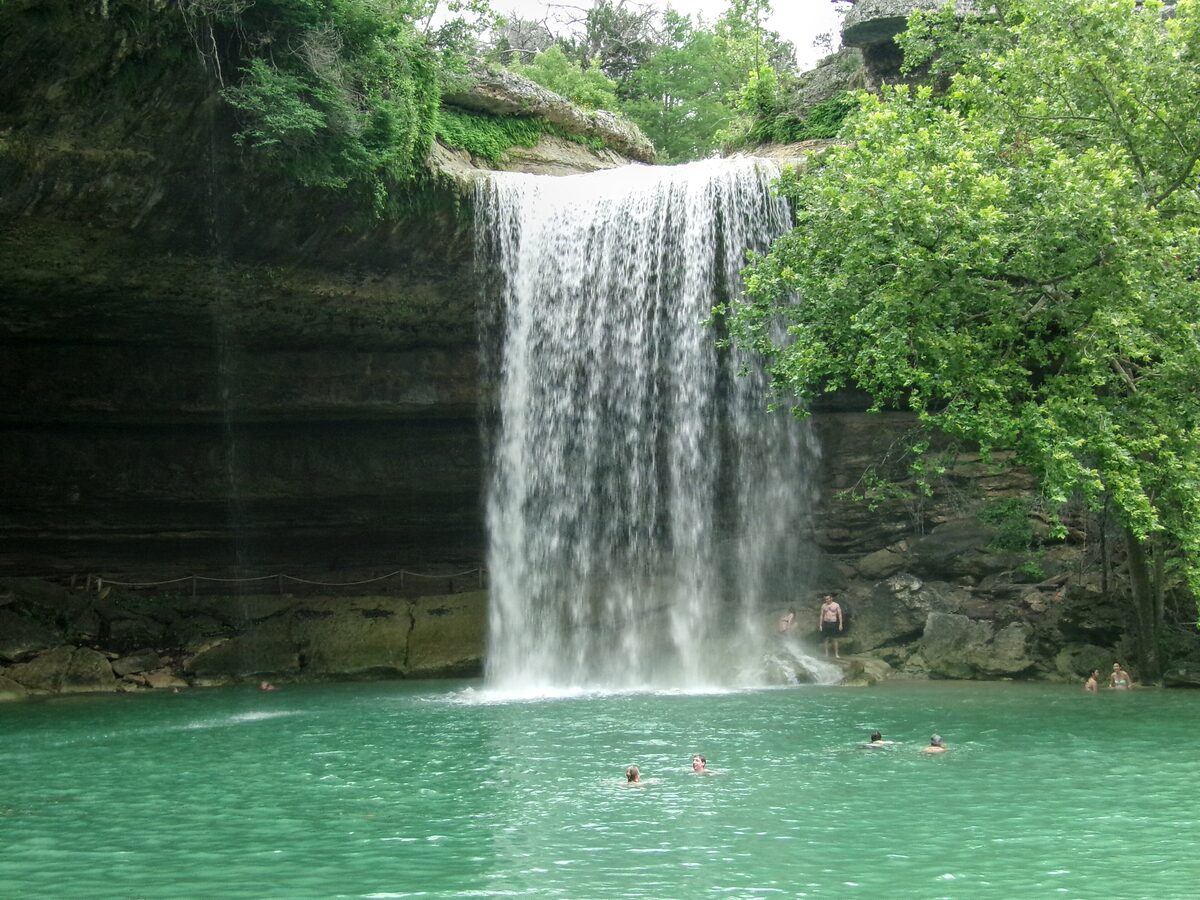 The waterfall at Hamilton Pool dropping into a turquoise pool with swimmers