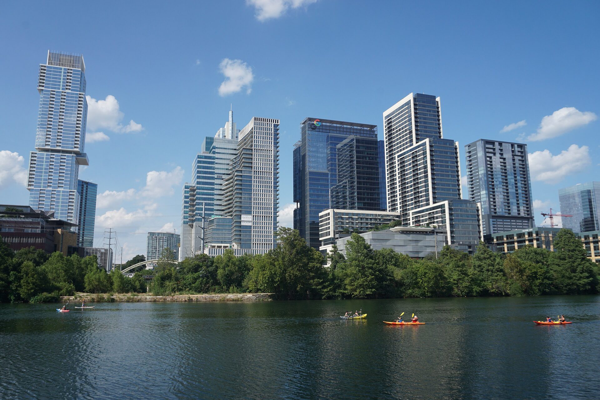 The downtown Austin skyline seen across Lady Bird Lake on a sunny day, with kayakers on the water