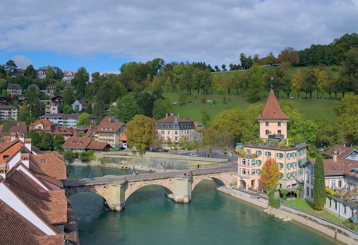 The green Aare under the Untertor bridge in Bern, with old-town roofs and autumn-coloured trees on the far bank