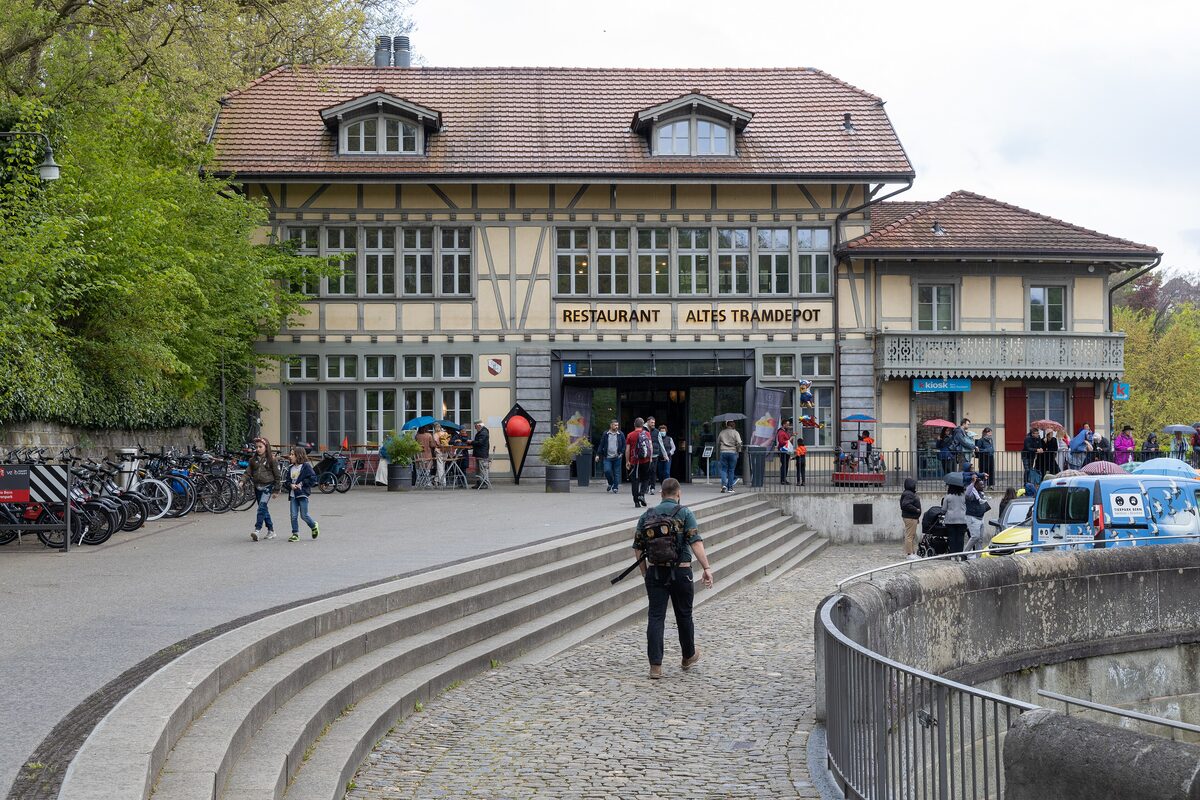 The half-timbered Restaurant Altes Tramdepot with its sign over the entrance, reached by wide stone steps, with outdoor tables and bicycles beside it