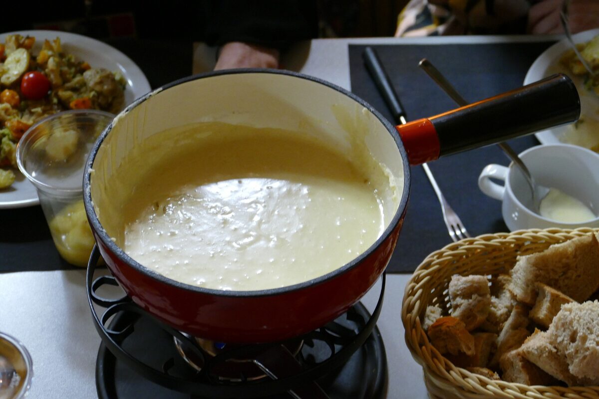 A red pot of melted cheese on a burner, with bread cubes in a basket beside it