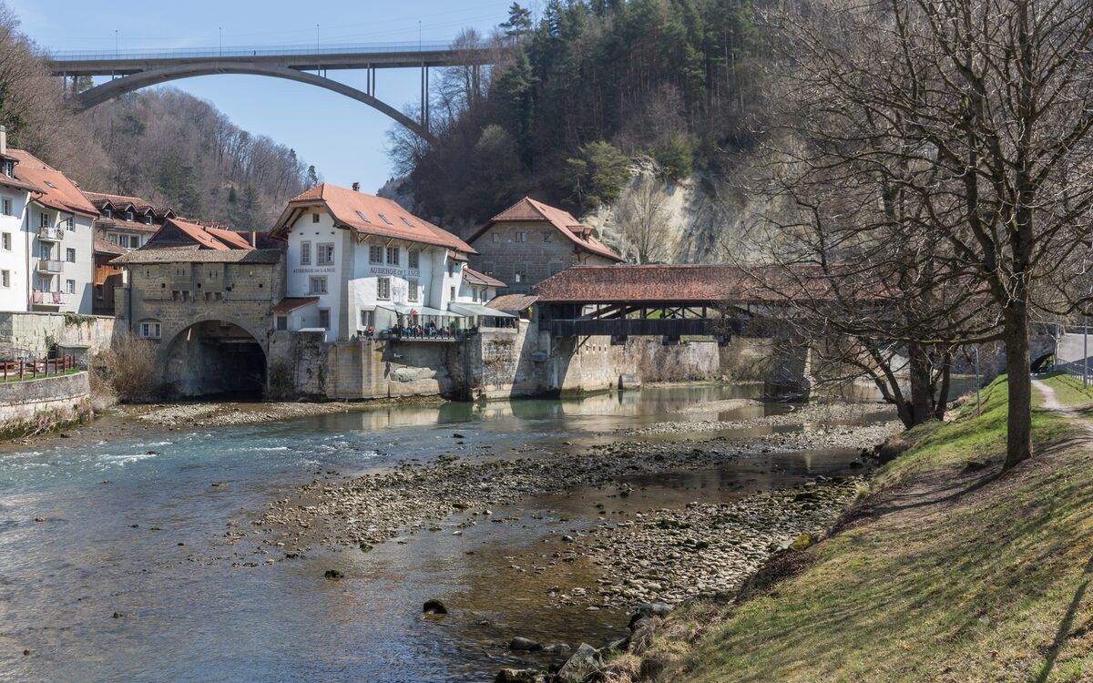 The Sarine in Fribourg's lower town, with the old covered bridge, stone houses and a high bridge above the trees