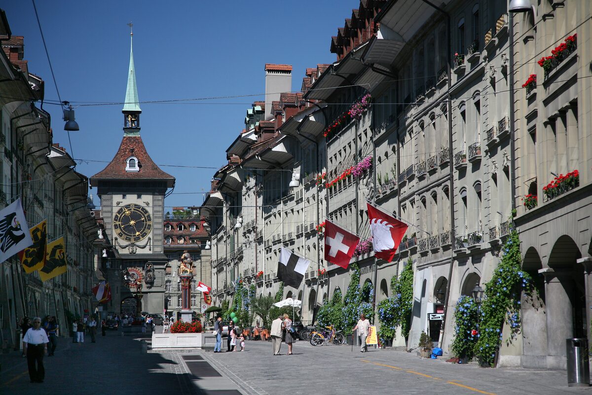 Kramgasse under its arcades, with the Zytglogge tower closing the street and Swiss flags on the house fronts