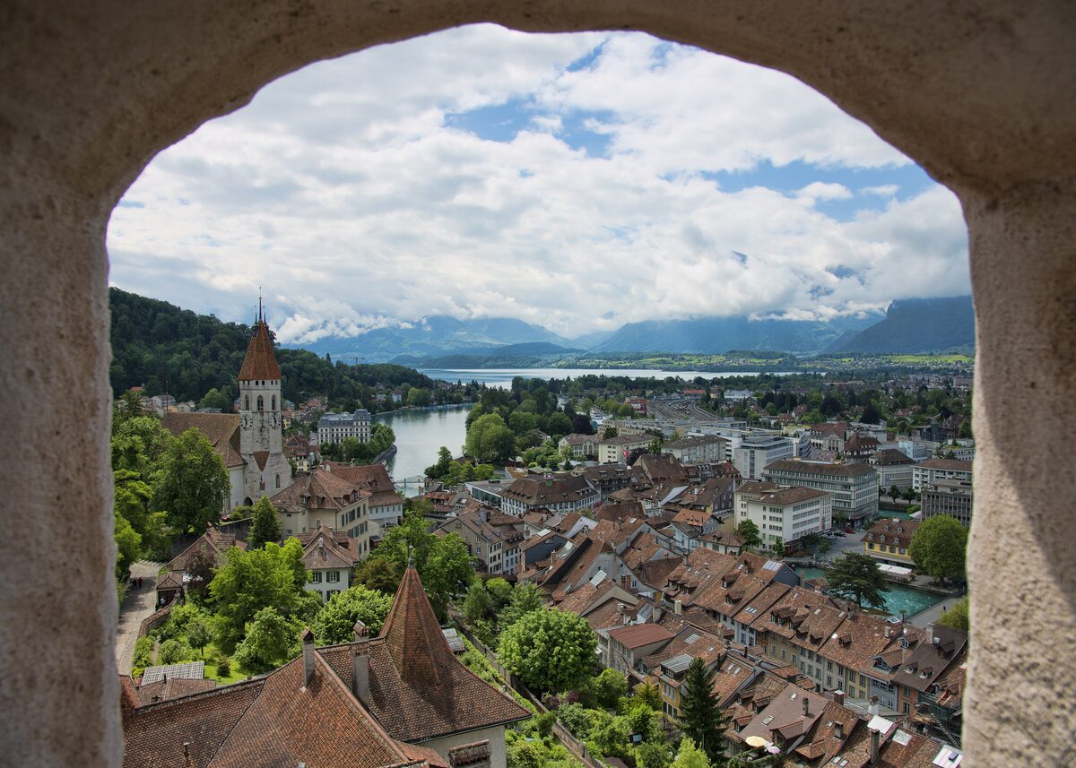 View through a stone arch from Thun Castle over the old town roofs, the river and the Alps