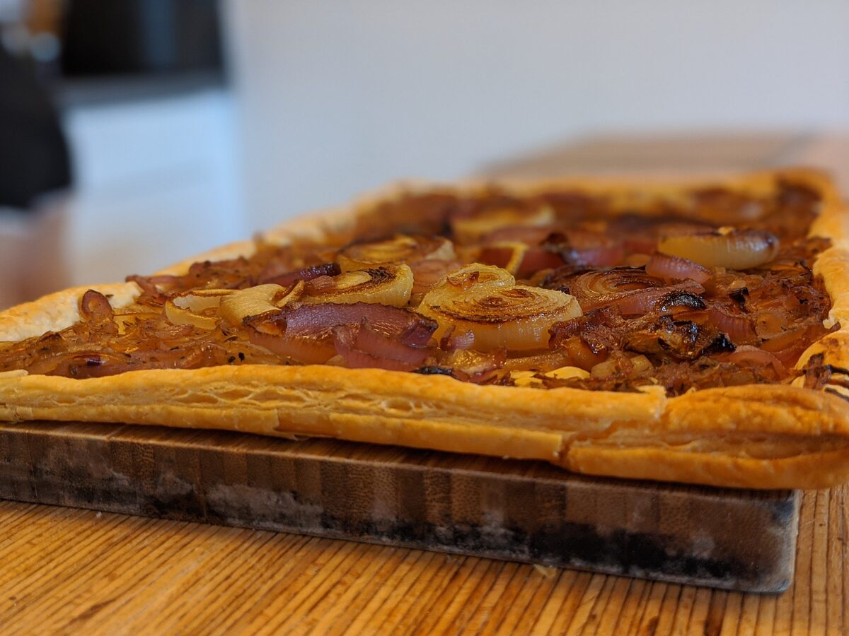A rectangular onion tart with a golden puff-pastry edge and caramelised onions on a wooden board