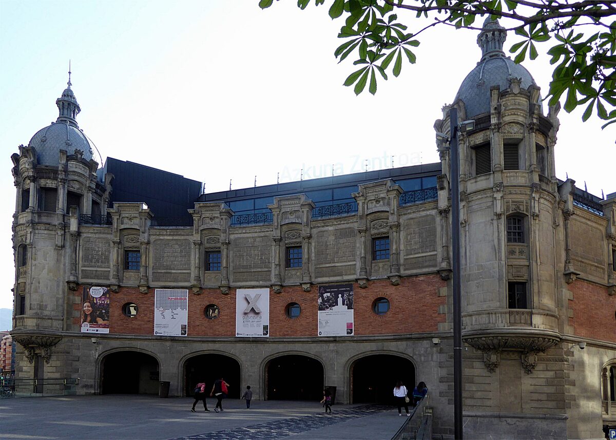 The brick and stone facade of Azkuna Zentroa, the former wine warehouse, with a domed corner tower at each end and arches at street level