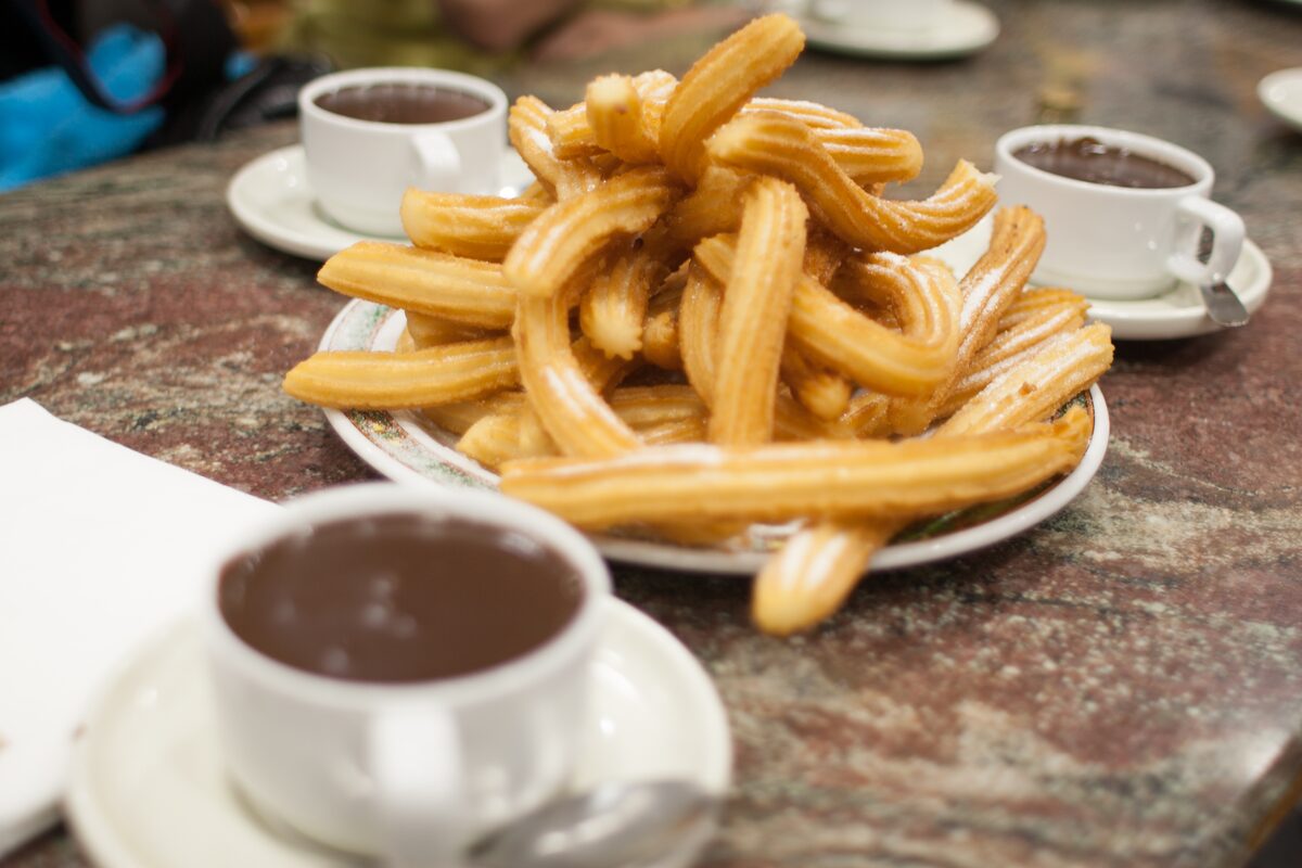 A plate of golden churros beside a cup of thick hot chocolate on a marble café table