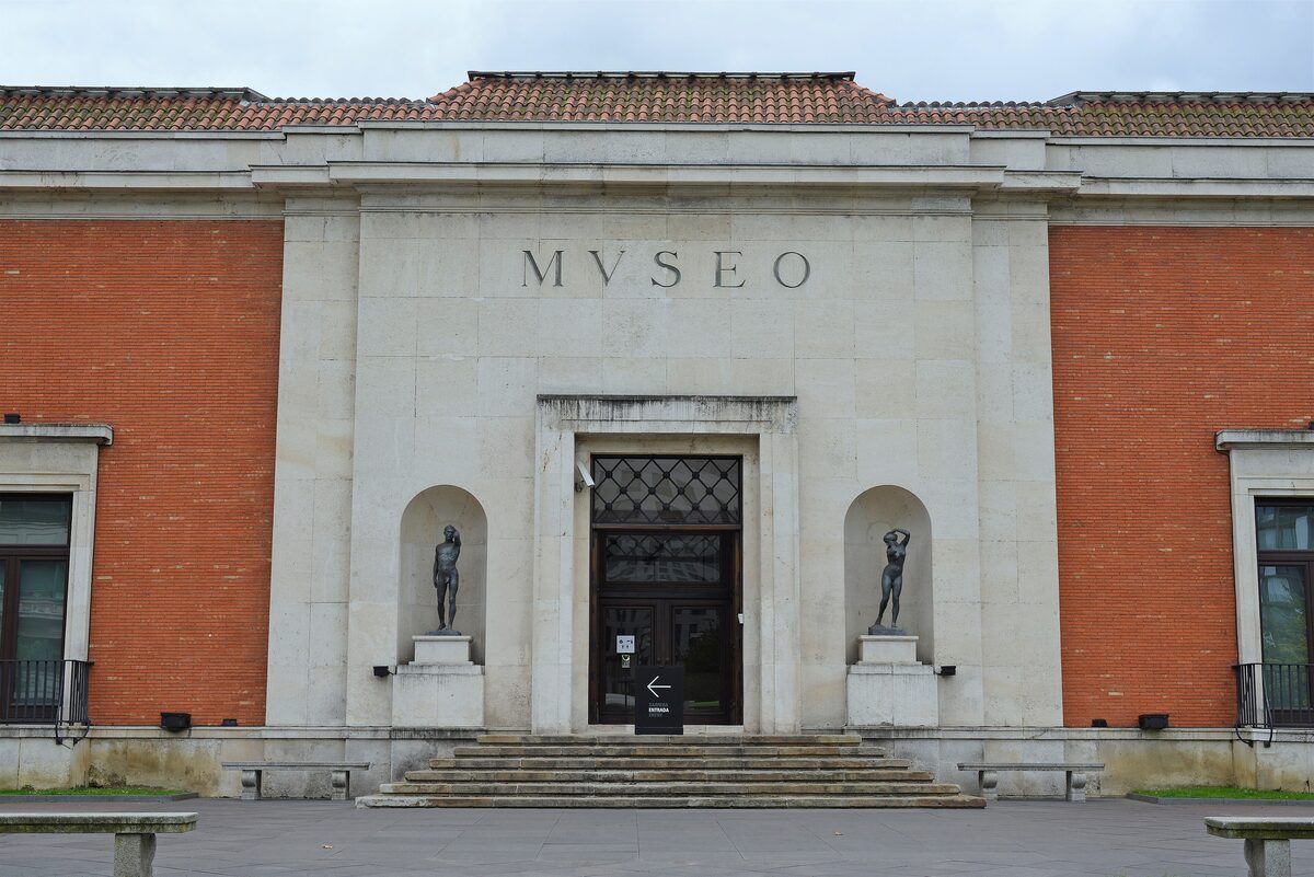 The brick and stone facade of the Bilbao Fine Arts Museum, with MUSEO over the entrance and two statues in niches
