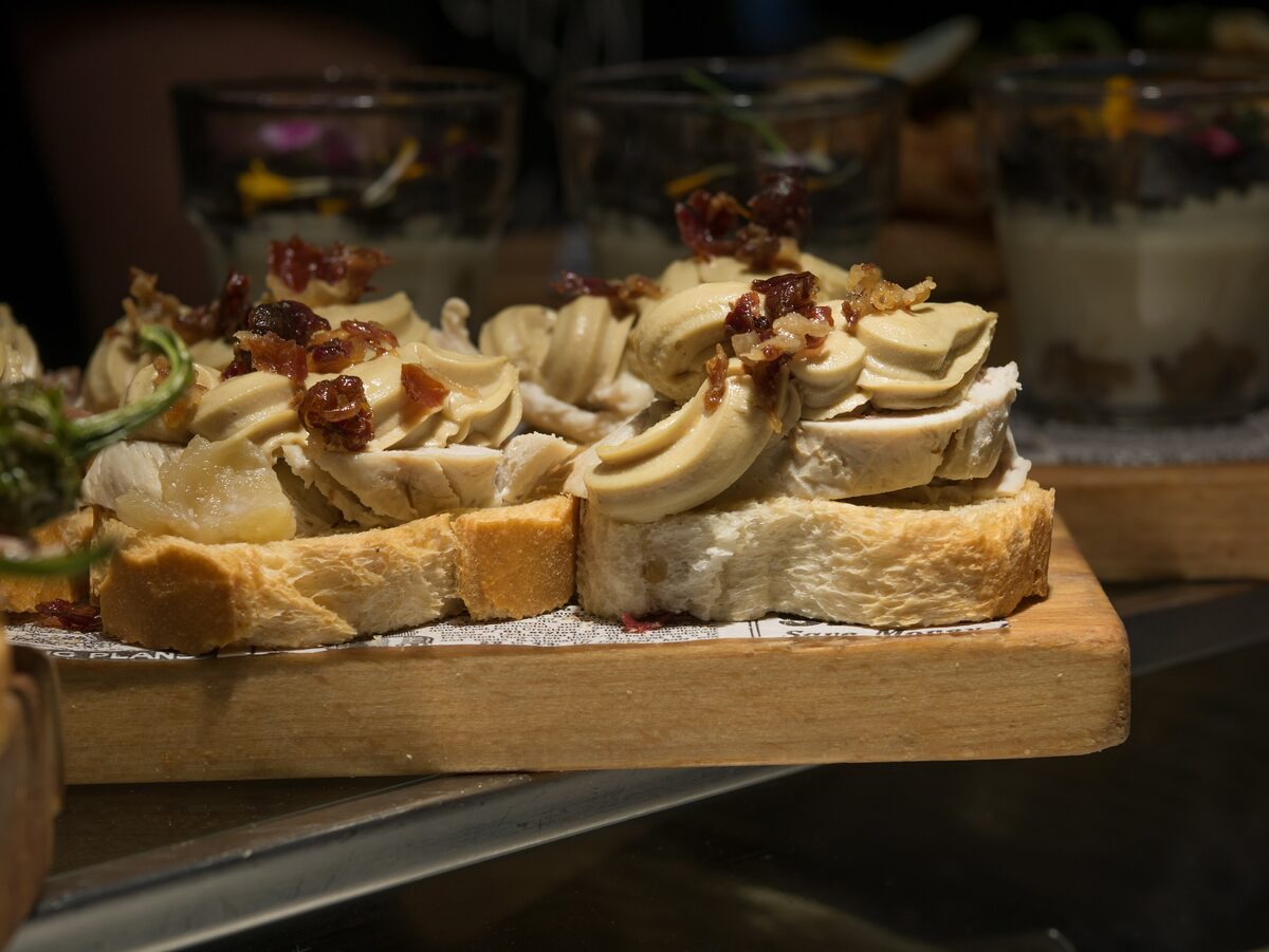 Bread pintxos with a creamy topping and crisp bits on a wooden board