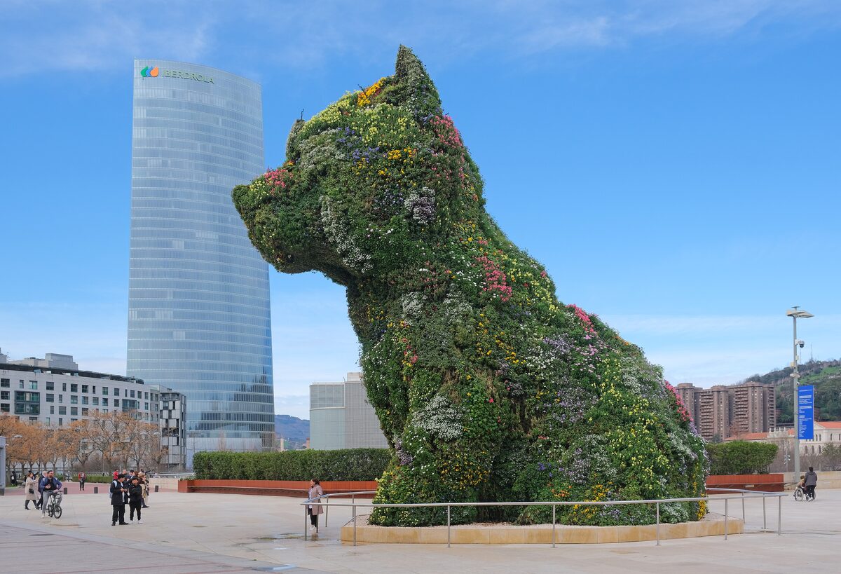 Puppy, Jeff Koons's terrier covered in flowers, on the plaza with a tall glass tower behind it