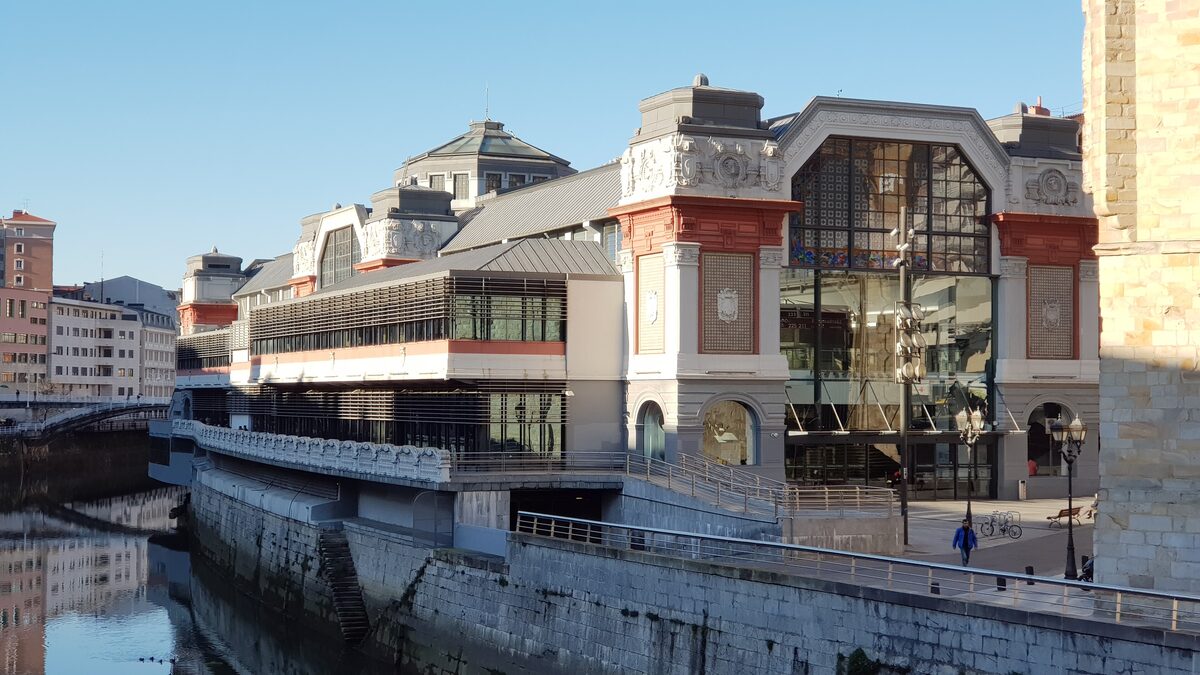 The Mercado de la Ribera market hall with its glass front and stone facade, seen from the riverside