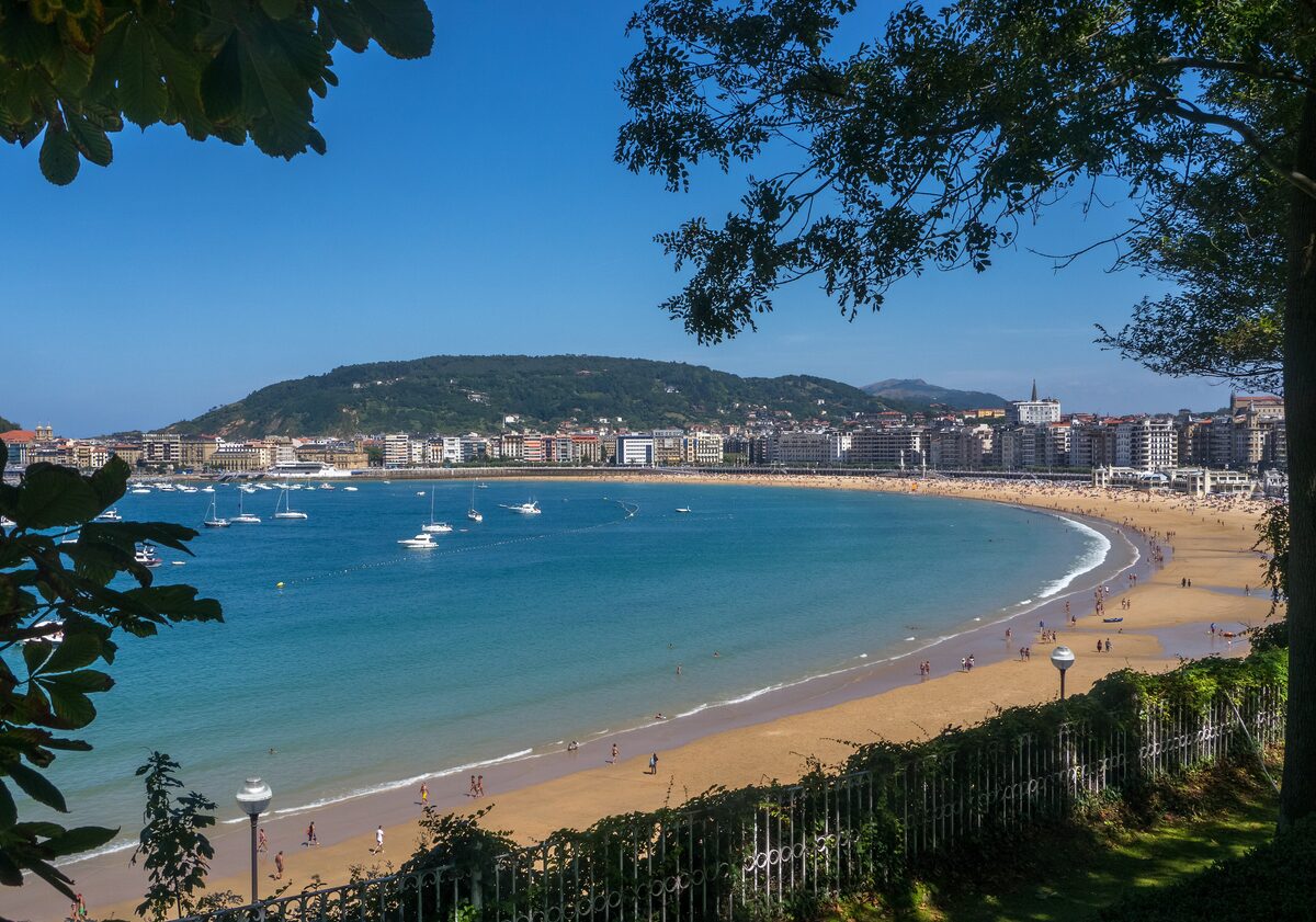 The curved sandy beach of La Concha in San Sebastián, with boats in the bay and green hills behind