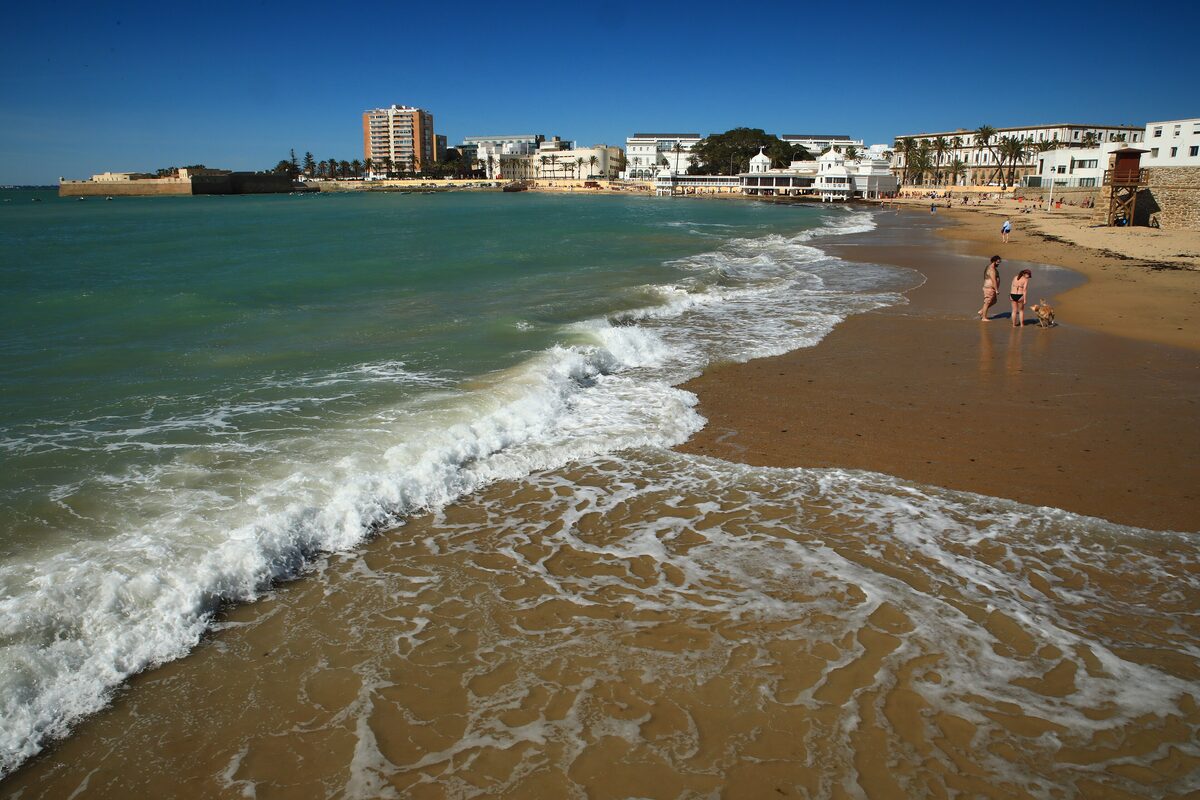 Waves and sand on La Caleta beach, with the town along the far shore