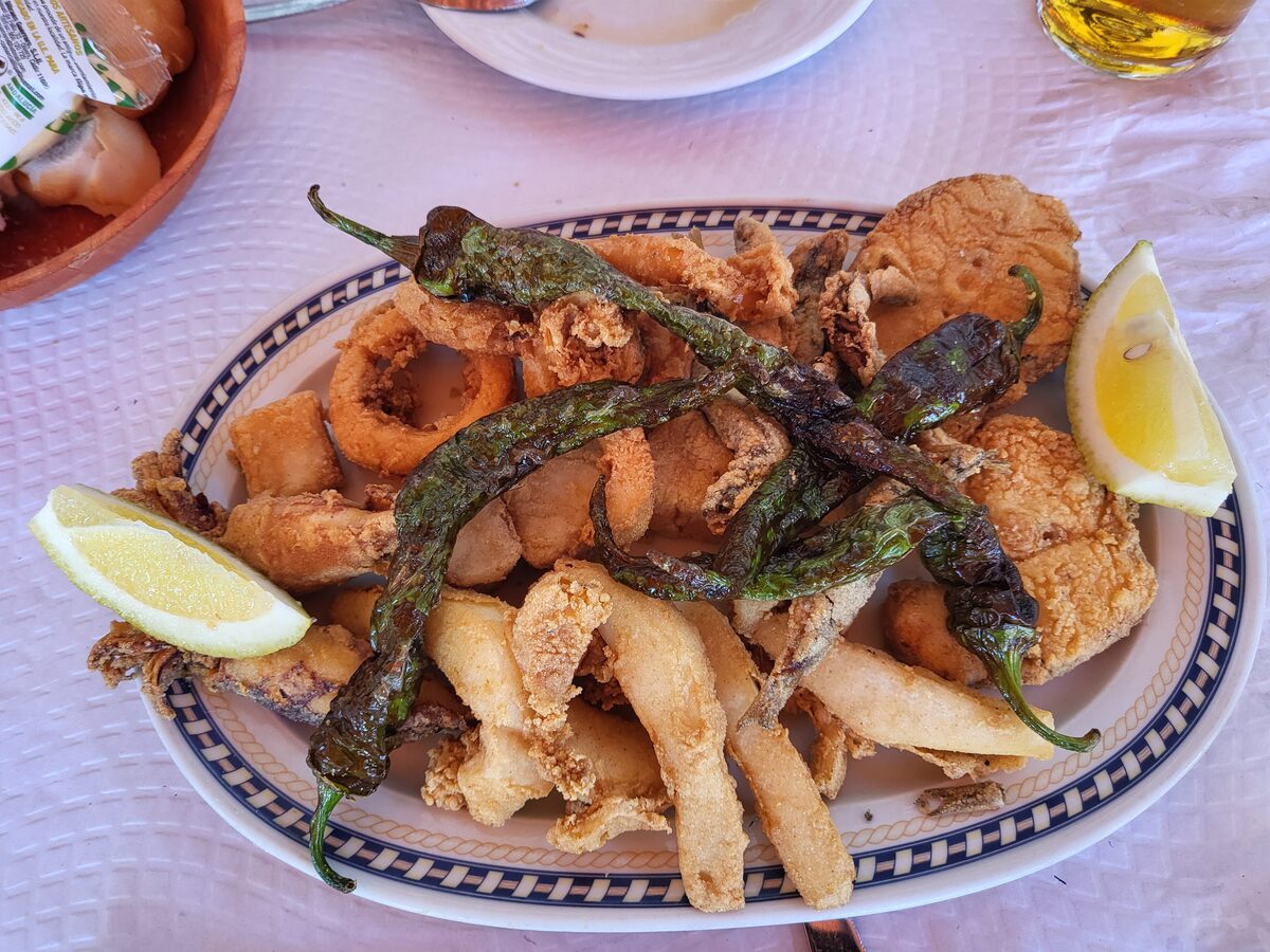 A platter of fried squid rings, fish and green peppers with lemon wedges on a patterned plate