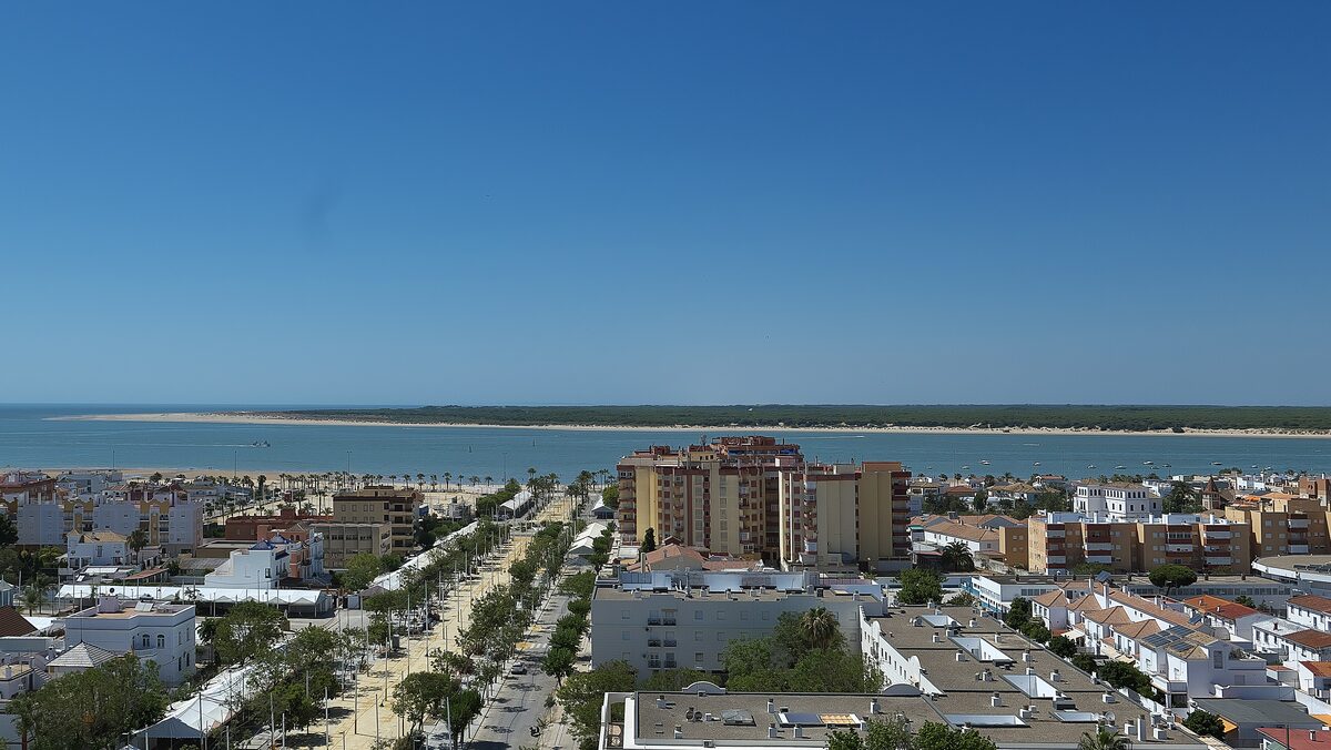 Sanlúcar's streets and apartment blocks beside the mouth of the Guadalquivir, with a sandbar under blue sky