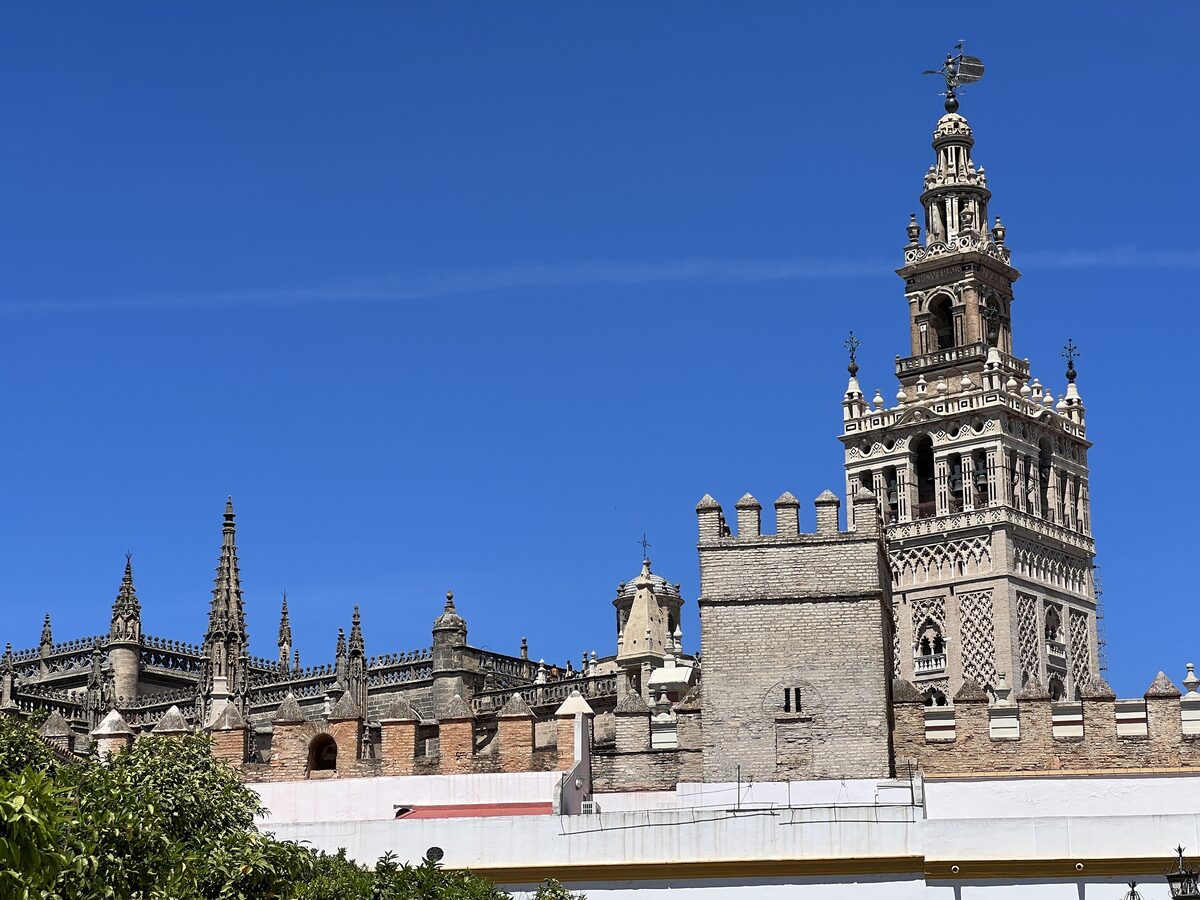 The Giralda tower rising above the cathedral roofline and battlemented walls in Seville, under a deep blue sky