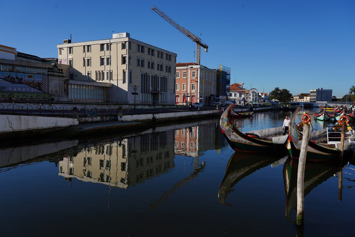Traditional moliceiro boats moored along a canal in Aveiro, with the buildings reflected in the still water