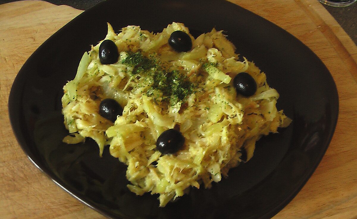 Bacalhau a Bras: shredded salt cod scrambled with egg and topped with black olives on a dark plate