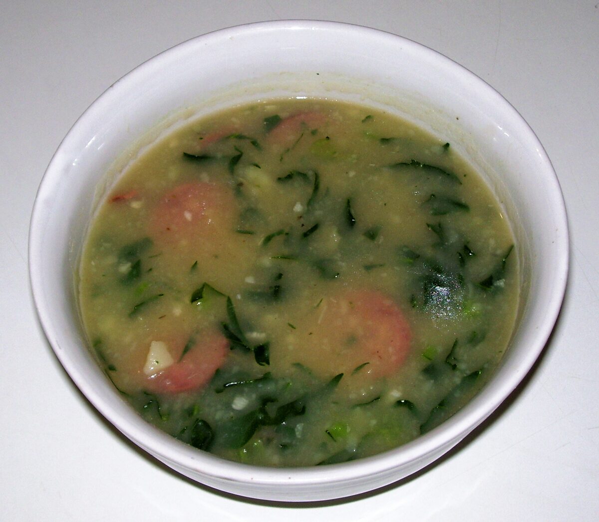 A white bowl of caldo verde, a green soup of shredded kale with slices of sausage