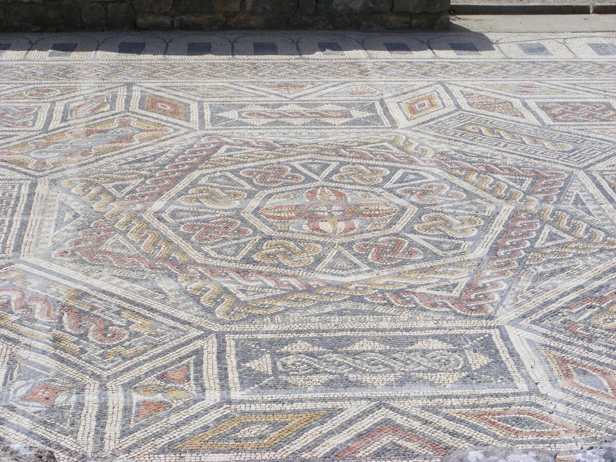 A Roman mosaic floor at Conímbriga with an eight-pointed star in the center and bands of geometric pattern in red, grey and white tesserae