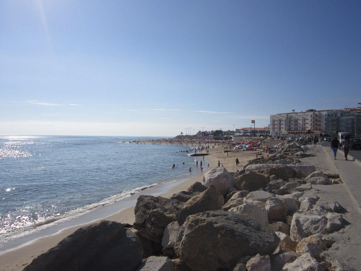 The sandy beach of Figueira da Foz with a rock breakwater in the foreground, bathers in the sea and buildings along the promenade