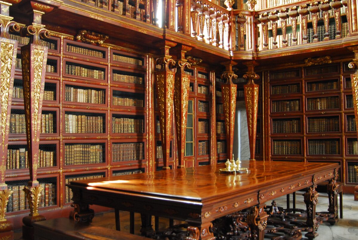 The gilded wooden shelves, carved columns and long wooden reading table of the baroque Joanina Library