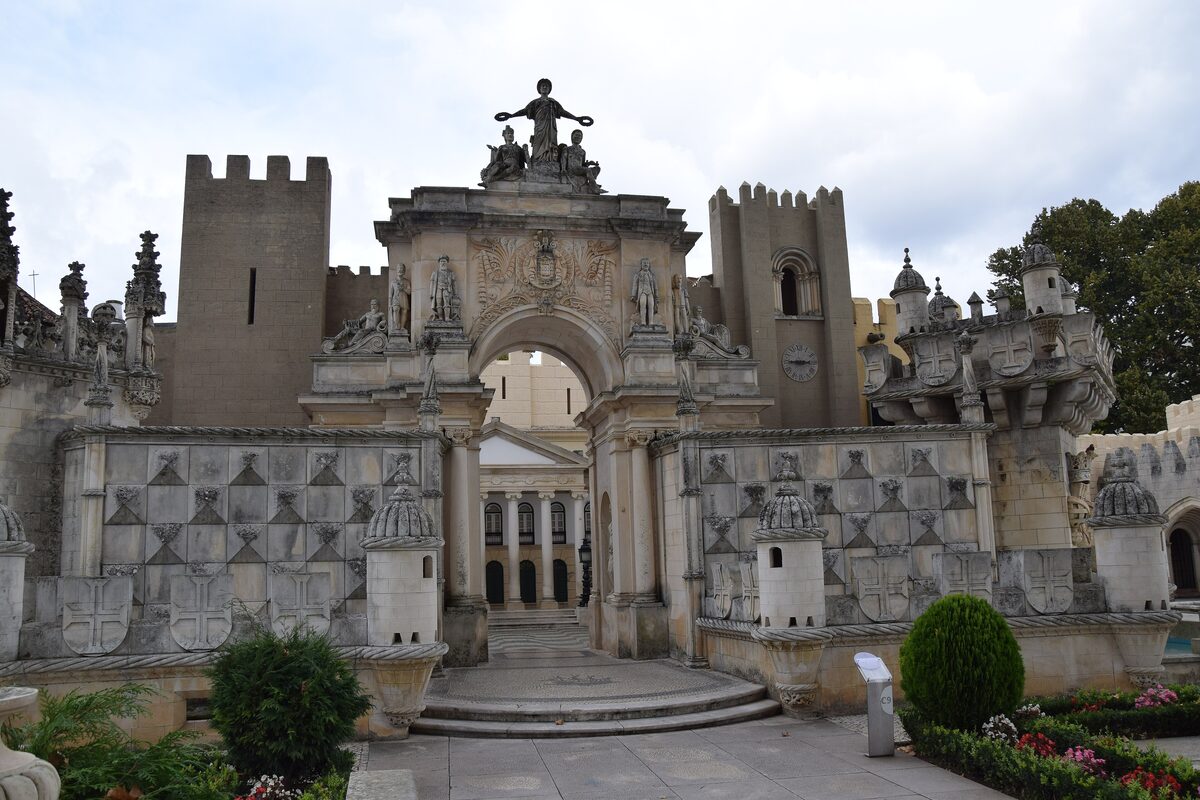 The crenellated white gate with a sculpted top and a carved arch at Portugal dos Pequenitos, with clipped shrubs and flower beds around it