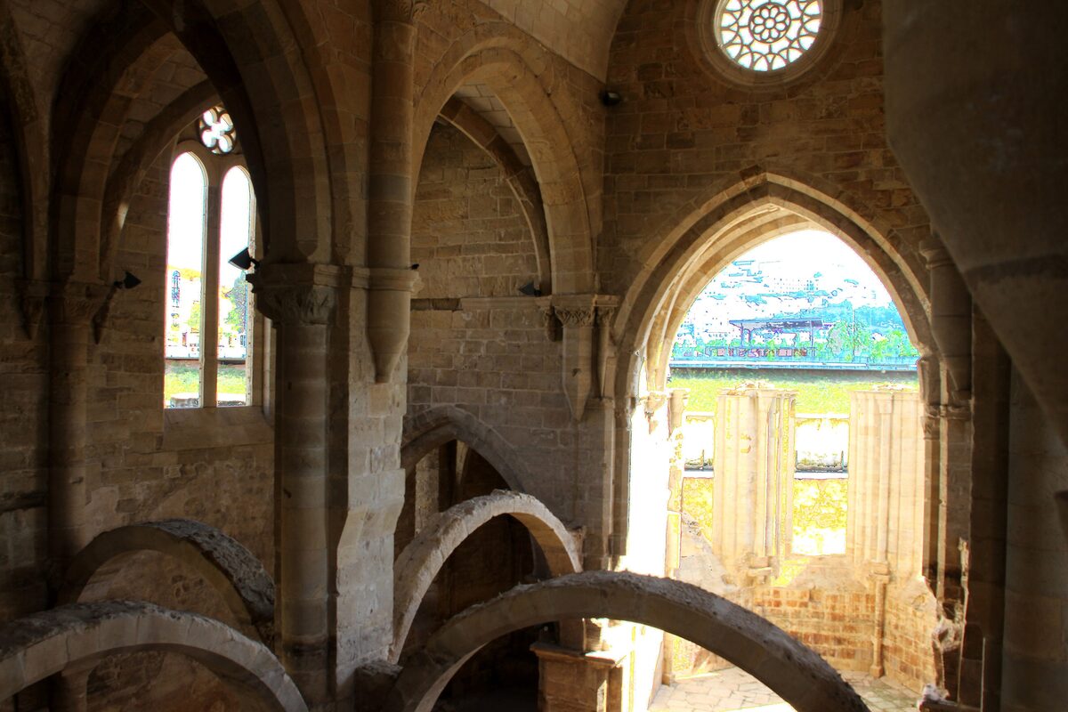 Inside the roofless Gothic church of Santa Clara-a-Velha: tall pointed arches, slender windows and a round rose window in pale stone, with the sunlit river valley seen through the end arch