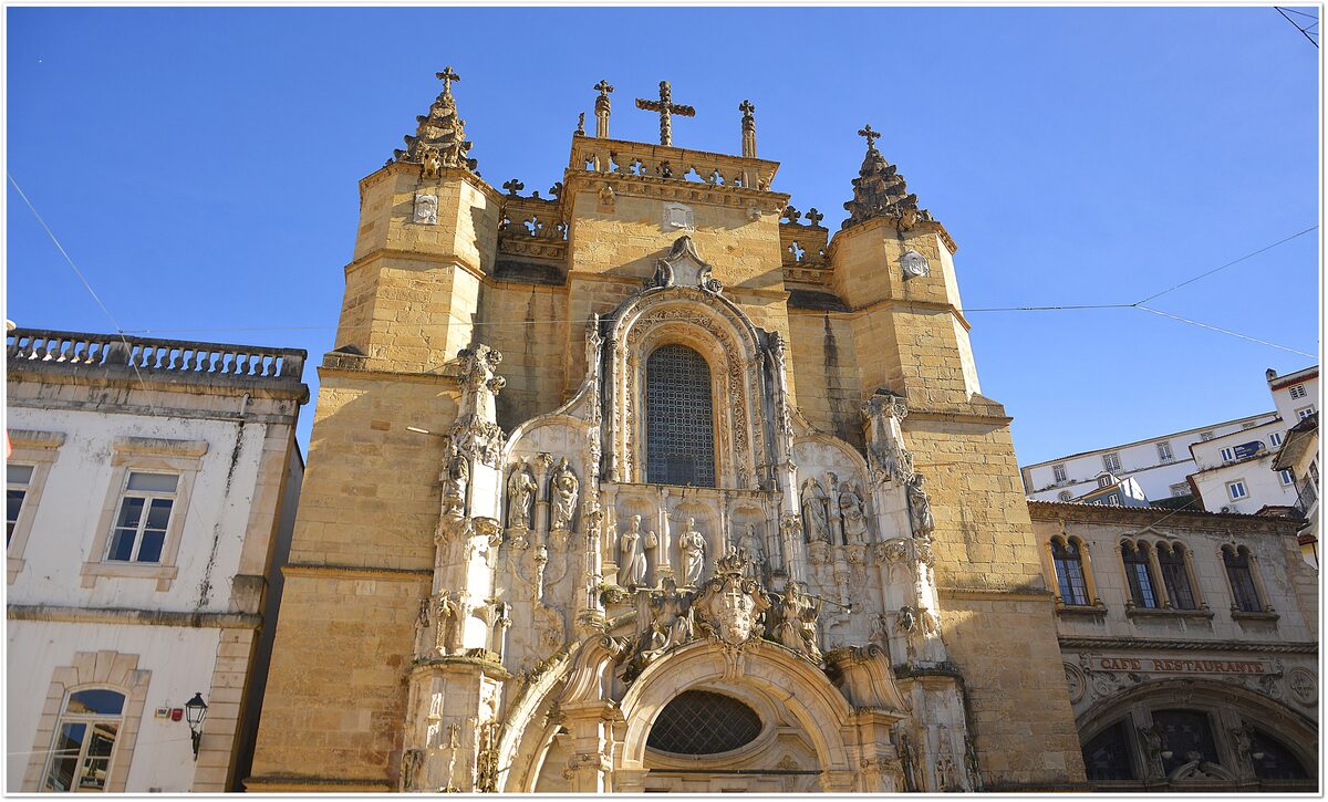 The ornate Manueline facade of the Santa Cruz Monastery church, with carved portal, pinnacles and two towers under a blue sky