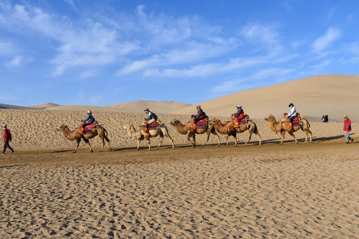 A string of riders on camels crossing the sand at Mingsha Shan in daylight