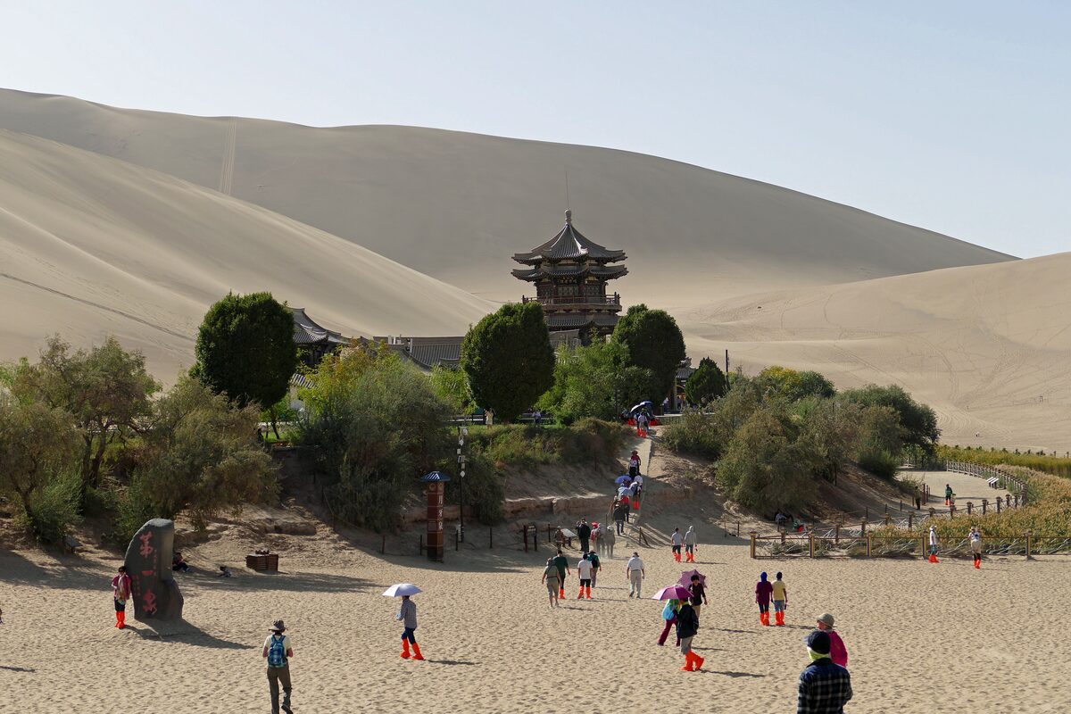 Visitors walking toward the trees and pagoda-roofed pavilion at Crescent Lake, with dunes rising behind