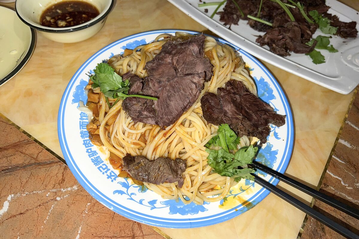 Yellow noodles topped with sliced donkey meat and coriander on a blue-and-white plate in Dunhuang