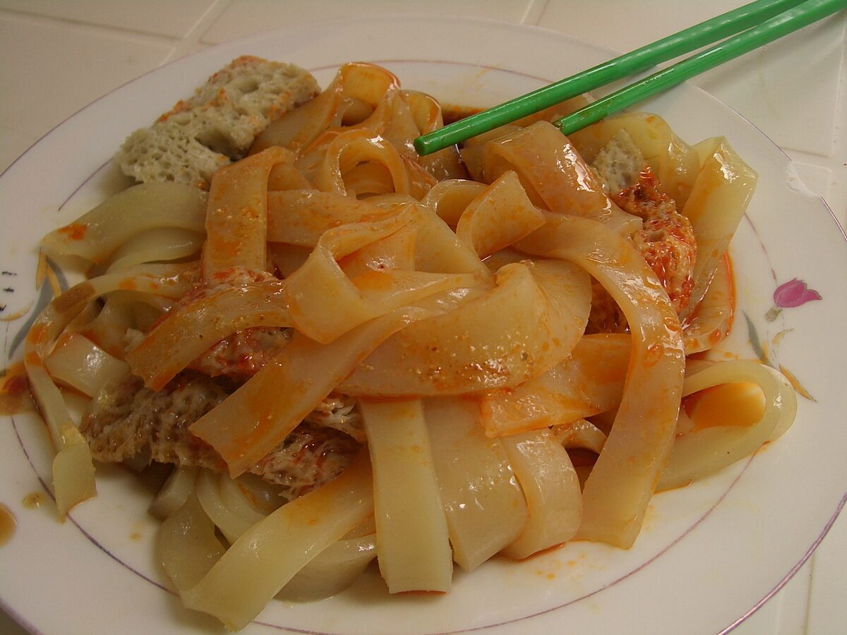 A plate of niangpi, wide chewy wheat-starch noodle sheets in red chili sauce, photographed in Linxia, Gansu