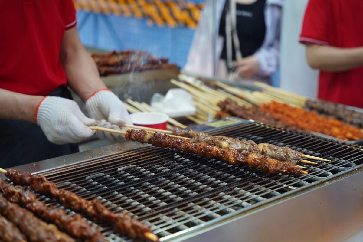 A gloved vendor turning meat skewers on a street grill, photographed at a stall in Shanghai