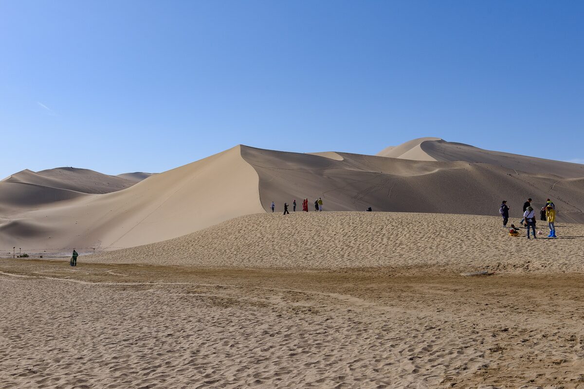 A tall dune ridge of Mingsha Shan under a blue sky, with a few walkers at its foot