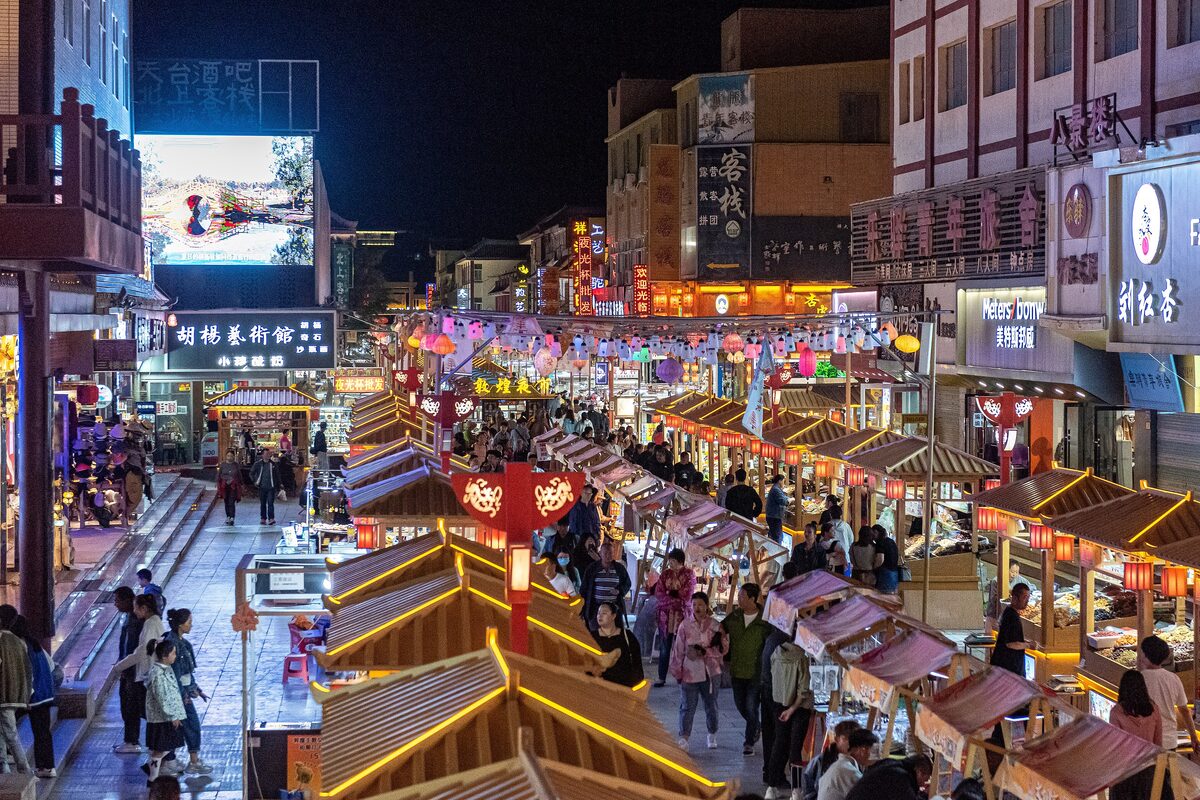 View down a street of lantern-lit stalls and shop signs at Shazhou Night Market after dark