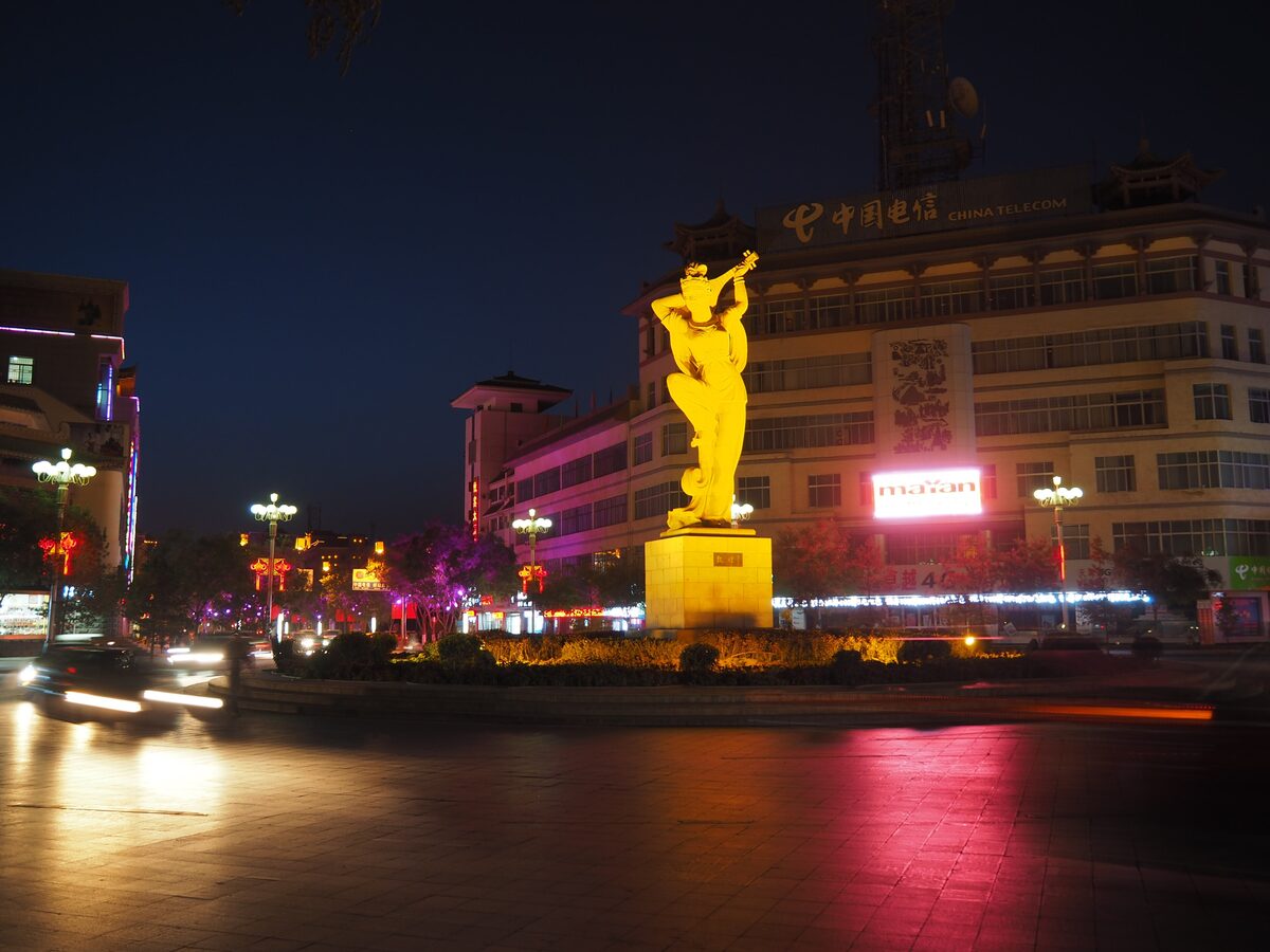 The golden statue of a dancer playing a pipa behind her back, lit up at night on a roundabout in Dunhuang